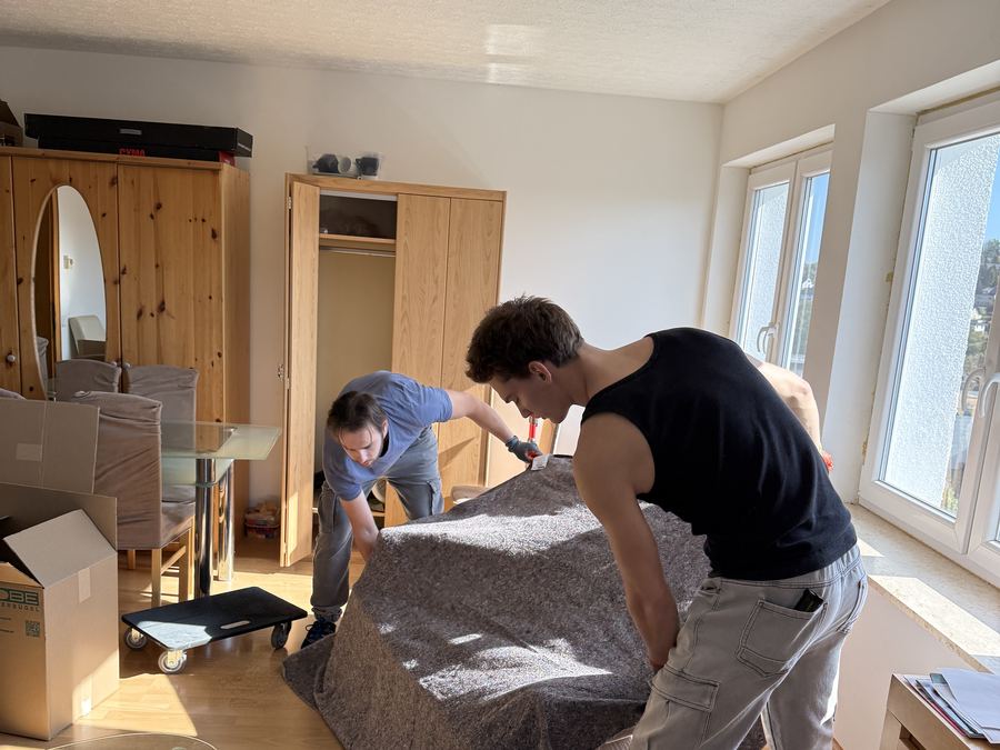 Zwei Umzugshelfer verpacken ein Sofa in Decken und Schutzfolie