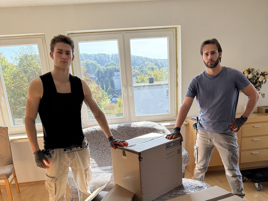 Zwei Umzugshelfer von Grundstein neben gepackten Umzugskartons in einer Wohnung